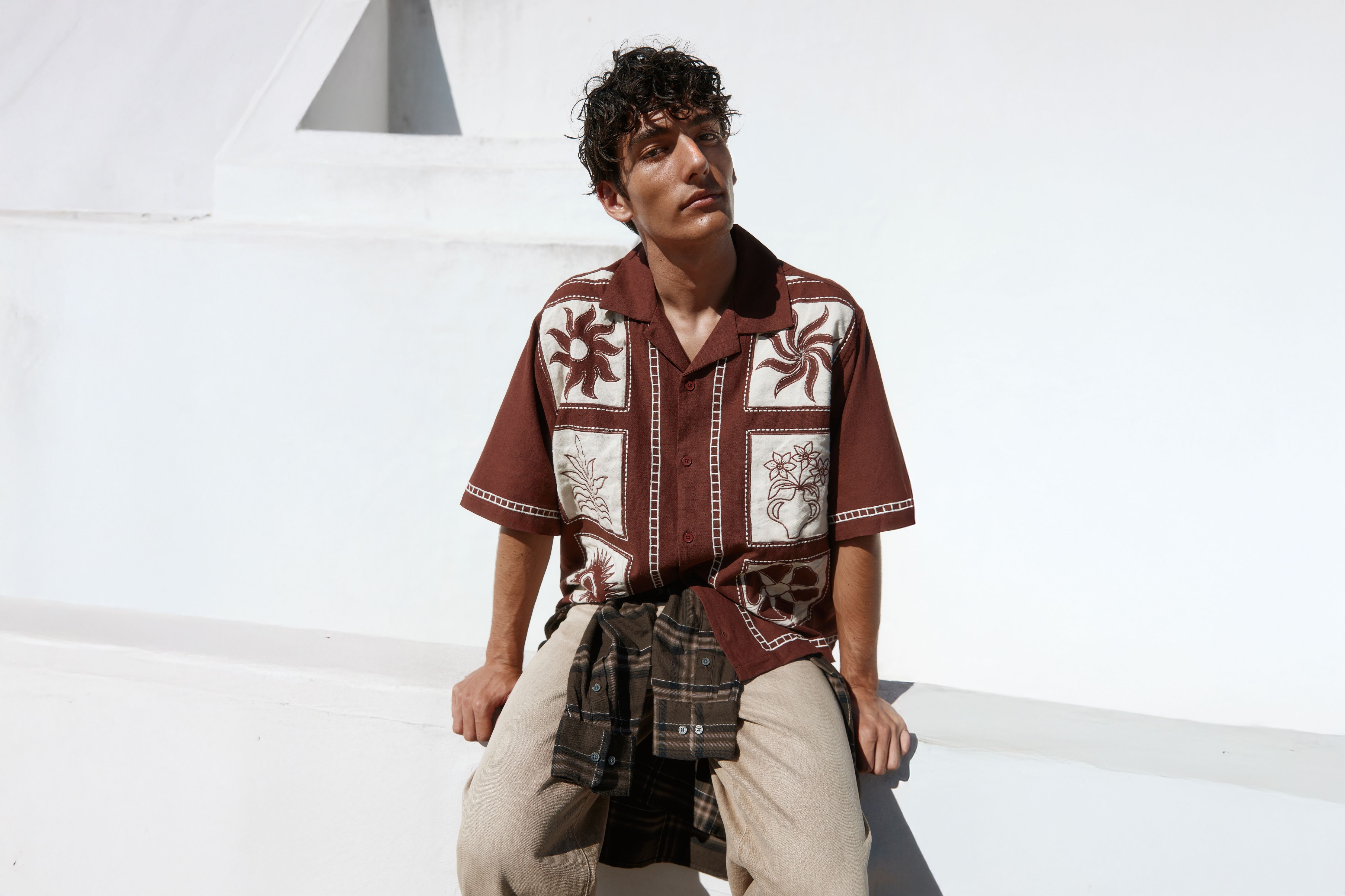 Homem sentado a usar uma camisa castanha de manga curta