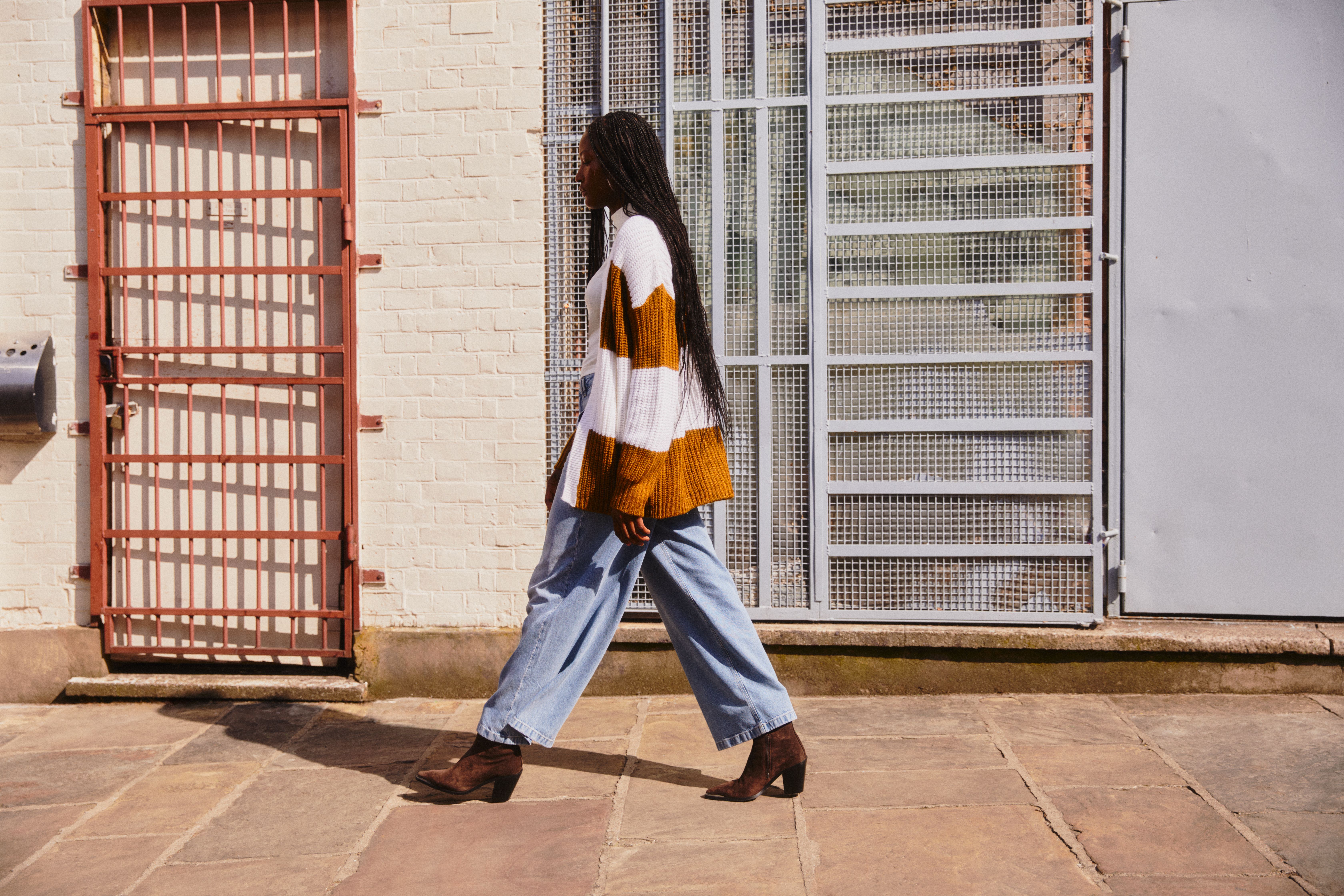 Mulher a passa, com umas calças de ganga largas e um casaco de malha.