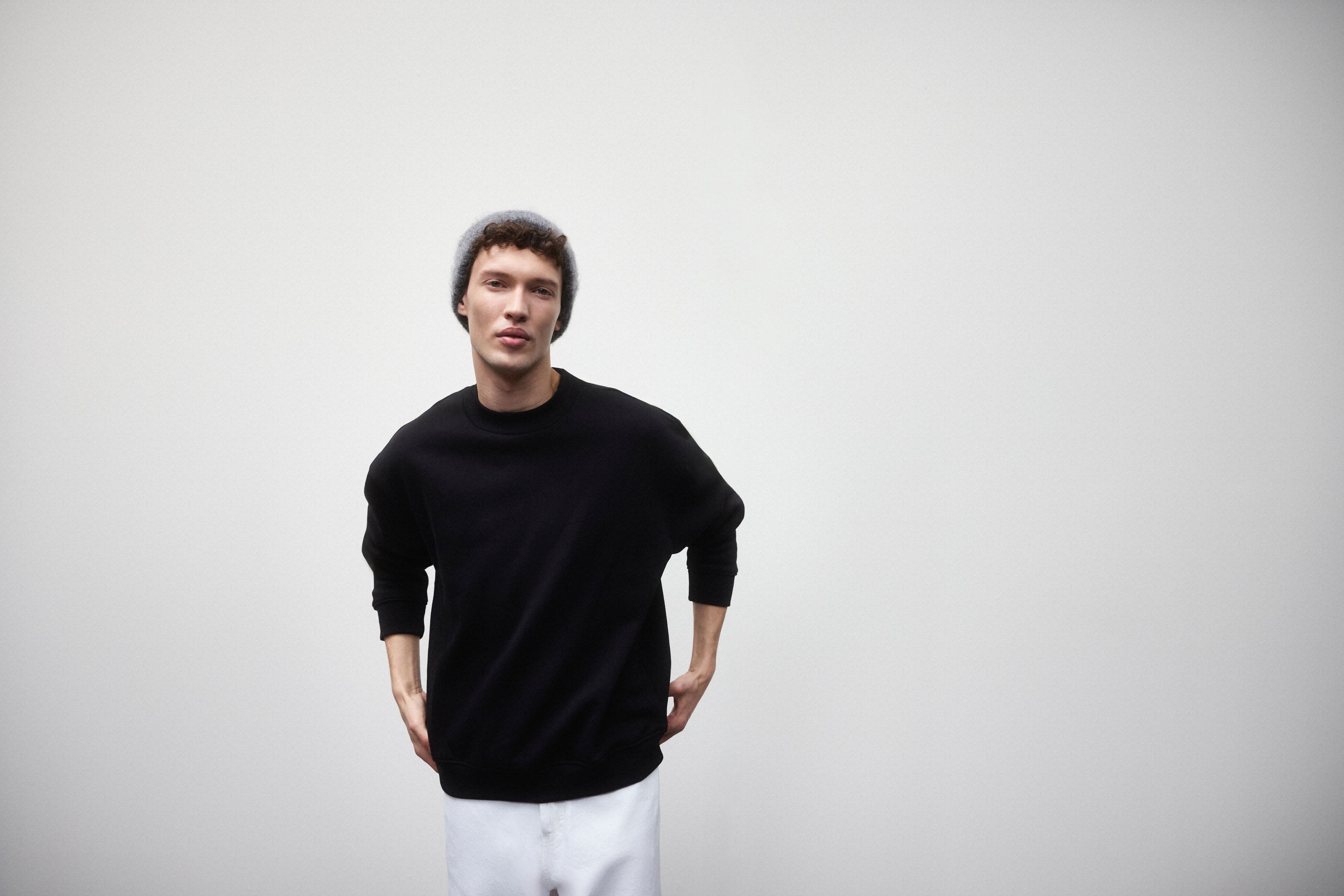 Homem a usar uma camisola preta, com calças de ganga brancas e gorro cinza